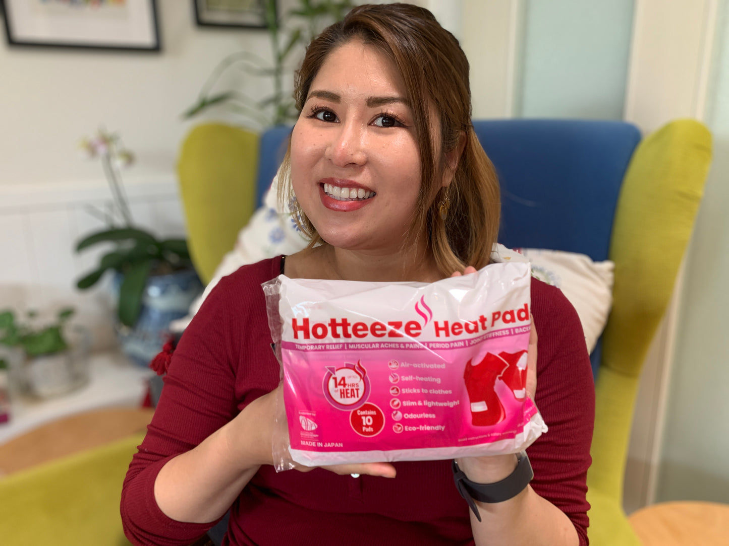 Woman smiling and holding a pack of Hotteeze Heat Pads, which contains 10 pads providing up to 14 hours of heat, in a casual indoor setting