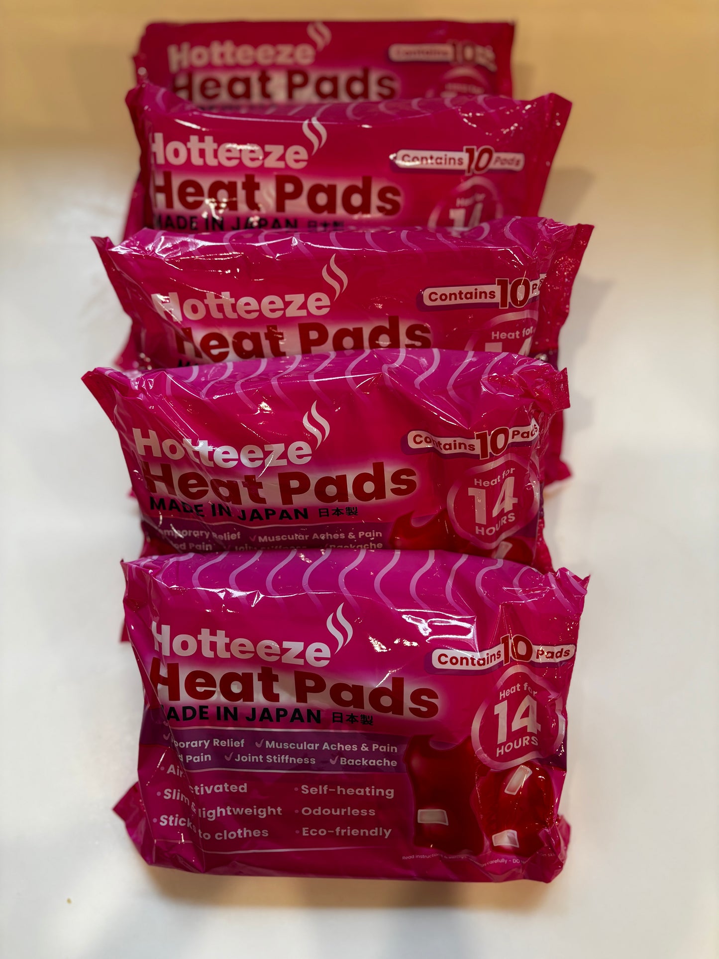 Five packs of Hotteeze Heat Pads, each containing 10 pads that provide up to 14 hours of heat, stacked in a row on a white background.